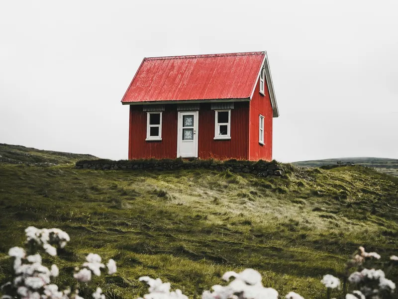 Casa de madera con techo rojo en medio de un campo del sur
